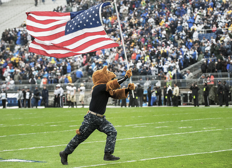 Nittany Lion mascot runs the field holding the American flag at a Military Appreciation football game. 